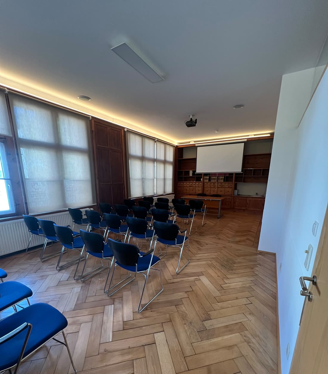 Der Seminarraum mit Leinwand, Bibliothekswand und Fischgrätparkett